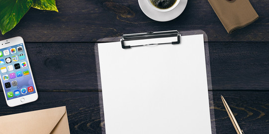 Tisch mit Schreibblock, Stift, Handy, Briefumschlag und Kaffeetasse