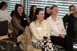 Foto: Mehrere Personen sitzen in drei Reihen hintereinander. Frauen in der ersten Reihe lachen.