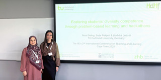 Photo: Sude Pekşen and Nina Bieling are standing in a conference room, next to them is a screen showing their presentation.