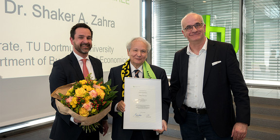 Gruppenfoto: Die Professoren Strese, Zahra und Bayer. Im Hintergrund: eine Leinwand sowie eine Fensterfront.