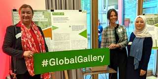 Gruppenfoto: Prof. Liudvika Leišytė, Nina Bieling und Sude Pekşen stehen vor dem Poster zum Projekt Future-AP und halten ein Banner mit der Aufschrift „#GlobalGallery“