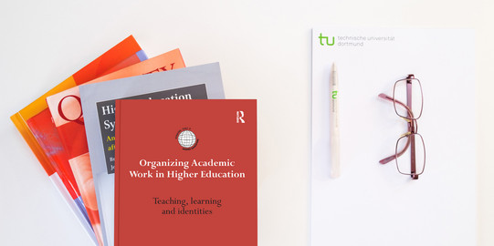 Stack of books, next to it a pad, a pen and glasses