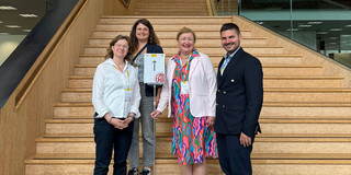 Gruppenfoto: Dr. Johanna Witte, Anna-Lena Rose, Prof. Liudvika Leišytė und Panourgias Papaioannou stehen auf einer Treppe, im Vordergrund ein Aufsteller mit dem EAIR-Logo.