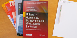 Photo: Stack of books, to the right a notepad with a ballpoint pen on it