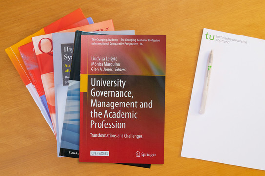 Foto: Bücherstapel, rechts daneben ein Block mit einem Kugelschreiber darauf