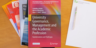 Photo: Stack of books, to the right a notepad with a ballpoint pen on it