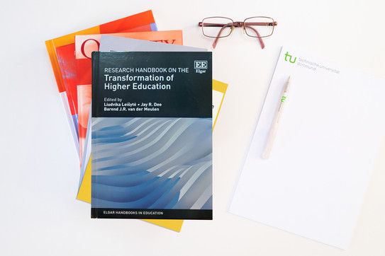 Research Handbook on the Transformation of Higher Education Foto: Bücherstapel, das oberste Buch ist das Research Handbook on the Transformation of Higher Education; daneben ein Block, ein Kugelschreiber und eine Brille