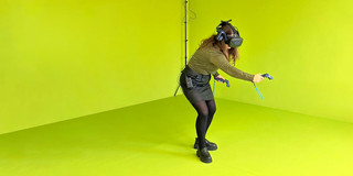 A woman in a greenroom with VR glasses and a controller