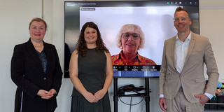 Group photo: Prof. Liudvika Leišytė, Anna-Lena Rose, and Prof. Uwe Wilkesmann stand in front of a screen showing Prof. Christine Musselin online