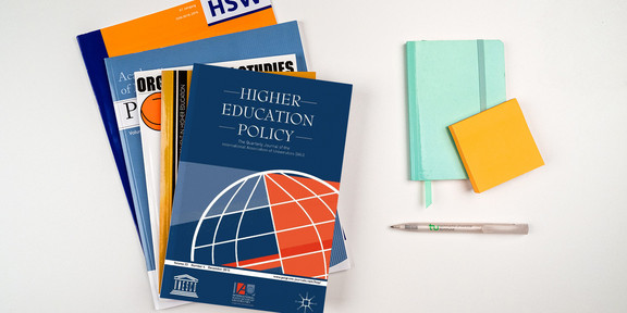 Zeitschriftenstapel, daneben ein Notizbuch und ein Stift