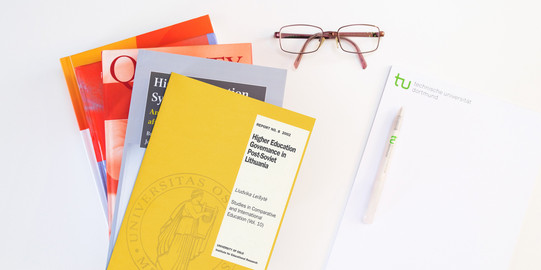Stack of books, next to it a pad, a pen and glasses