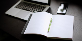 Turned on laptop, smartphone and notebook with pen lying on a table.
