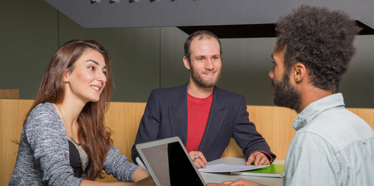 Three students sit opposite each other and they are talking.