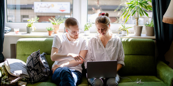 Zwei Studierende arbeiten am Laptop, auf einem Sofa sitzend.