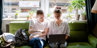 Zwei Studierende arbeiten am Laptop, auf einem Sofa sitzend.