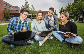 Four students are sitting on the grass and looking in a book.